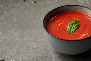 plate of appetizing tomato soup with basil on grey table