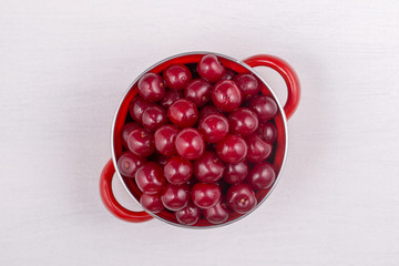 Red cherries in red enamel saucepan on white background
