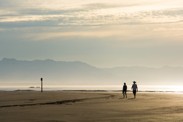 Casal caminhando na Praia da Enseada, ao amanhecer