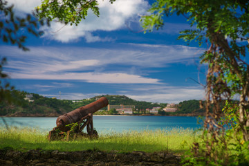 Old cannon in the fort is looking at sea with amazing clouds and island on background