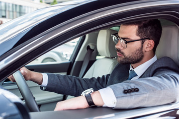 side view of businessman in eyeglasses driving car