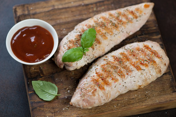Closeup of bbq turkey breast fillet with sauce on a rustic wooden serving board, horizontal shot