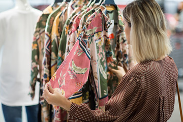 Young woman choosing clothes in mall or clothing store - Shopping, fashion, style and people concept