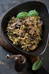 Close-up of bulgur with fried champignons served in a black bowl, selective focus, vertical shot