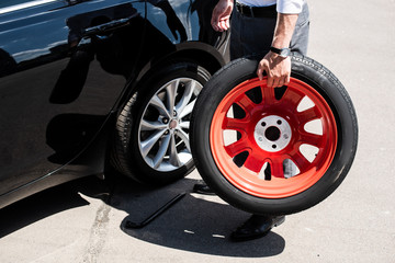 Fototapeta na wymiar cropped image of businessman holding tire for wheel replacement at street