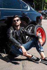 Fototapeta na wymiar tired stylish man in sunglasses sitting near broken car at street