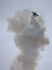 Sportowy samolot w powietrzu wykonuje akrobacje pozostawiając za sobą ciemny dym
