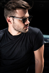 Obraz premium side view of stylish man in sunglasses in front of car with opened bonnet