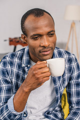 pensive young african american man holding coffee cup at home