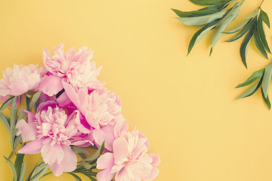 Bouquet of pink peonies on a yellow surface in vintage toned, top view, copy space