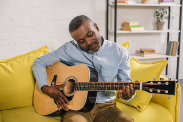 smiling african american man playing acoustic guitar at home