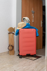 Fototapeta na wymiar Red suitcase for summer holidays in front of an opened apartment door