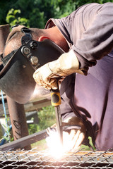Welder welding  a metal part wearing standard protection equipment