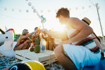 Group of friends making party on the beach at sunset time