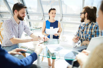 Young businesswoman with papers talking to her colleagues or answering their questions after making report