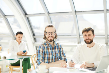 Young creative businessmen sitting by table in front of laptop and working over new ideas