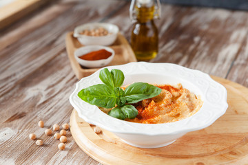 Fresh classic hummus with basil in the bowl on wooden background
