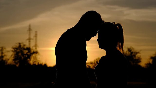 A silhouette of a loving couple. Young man comes to a young woman and hugs her. They marrily stand, holding hands