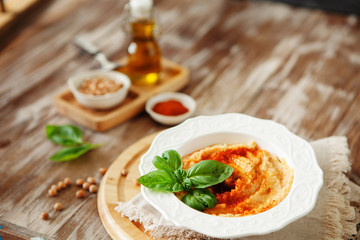 Fresh classic hummus with basil in the bowl on wooden background