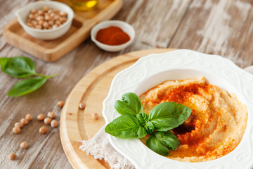 Fresh classic hummus with basil in the bowl on wooden background
