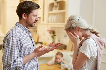 Obraz premium Annoyed husband expressing his displeasure to crying wife with their little daughter on background