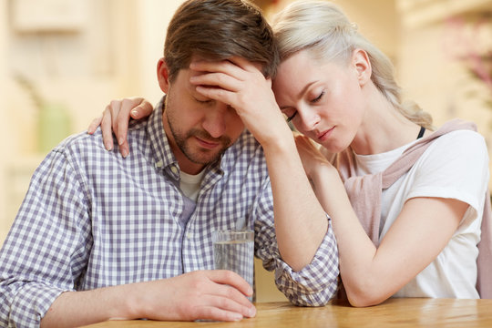 Young Troubled Couple Sitting By Table While Surviving Hard Times Of Their Family Life