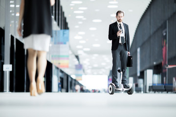 Busy young agent in suit reading message in smartphone while moving on gyroscope