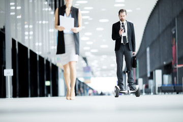 Young man in suit concentrating on texting in smartphone while moving forwards on hoverboard