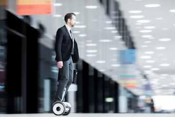 Obraz premium Young businessman on hoverboard hurrying for briefing or conference inside modern building