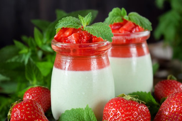 Two layered panna cotta with matcha tea topped with strawberry jelly, berries and mint in glass jars