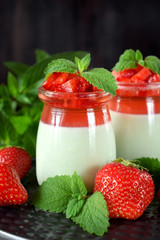 Two layered panna cotta with matcha tea topped with strawberry jelly, berries and mint in glass jars