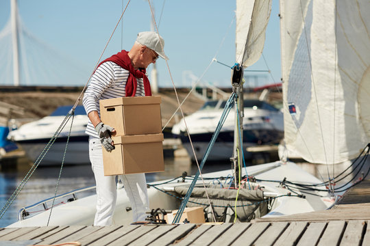 Senior man in casualwear carrying packed boxes while working on his yacht on summer day