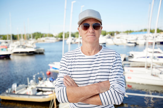 Senior cross-armed yachtsman in sunglasses and striped singlet standing in front of camera