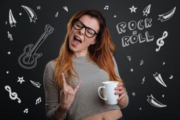 Rock music. Emotional young woman closing her eyes and holding a cup of coffee while enjoying amazing rock music