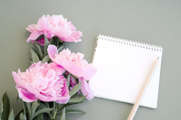 Bouquet of pink peonies, empty open notebook for your inscription and a pencil on a gray background, top view