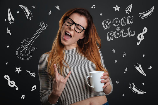 Rock music. Emotional young woman closing her eyes and holding a cup of coffee while enjoying amazing rock music