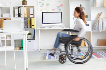 Blurry silhouette of office worker moving on wheelchair inside modern office
