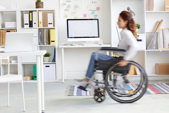 Blurry silhouette of office worker moving on wheelchair inside modern office