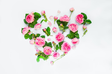 Creative layout with pink tea rose flowers, petals and leaves in shape of heart on white background isolated. Summer, spring love concept. Top view. Flat lay. Selective focus, copy space.