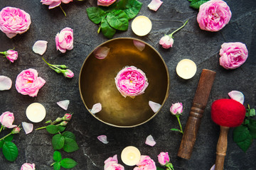 Tibetan singing bowl with floating rose inside. Burning candles, tea rose flowers and petals on the...