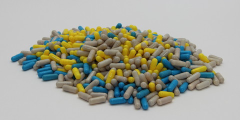Scattered multi-colored pills – blue, gray and yellow capsule, close-up on white background