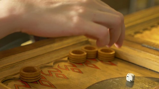 Detail of a backgammon game with two dice close up. Female and male hands rolling two dice and moving checkers on board. Young people playing backgammon while relaxing. 4k, slow motion