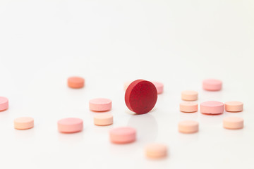 Multiple pink and red pills on a white background with several of them out of focus. Medications in the form of tablets.