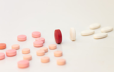 Multiple white and pink and red pills on a white background with several of them out of focus. Medications in the form of tablets.
