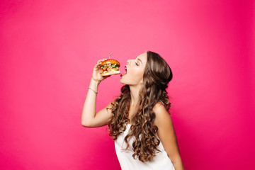 Hungry girl with opened mouth eating big hamburger.