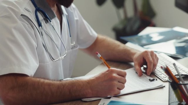 Caucasian doctor with stethoscope on neck sitting at table in doctor&rsquo;s office, shaking patient&rsquo;s hand. Indoors. Popular clinic of the city.