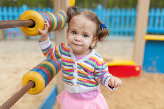 a little girl with two tails is dressed in a striped colorful jacket is playing in the sandbox on the playground