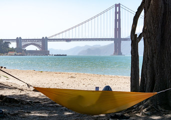 Person lays in hammock while reading book with the Golden Gate Bridge in the distance