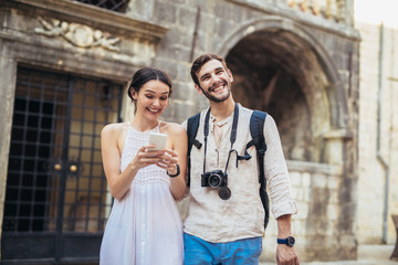 Naklejka premium Traveling couple of tourists walking around old town, and using smart phone. Vacation, summer, holiday, tourism: concept.