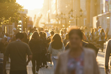 Silhouettes of people crowd walking down the street at summer evening, beautiful light at sunset